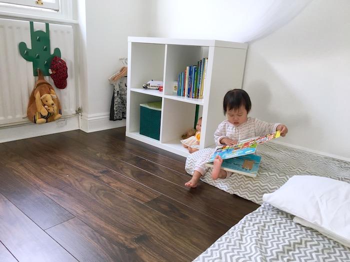 dvi lovos ant grindų su pilka ir balta „Chevron“ antklode, rudas parketas, „Kallax“ lentyna knygoms ir žaislams