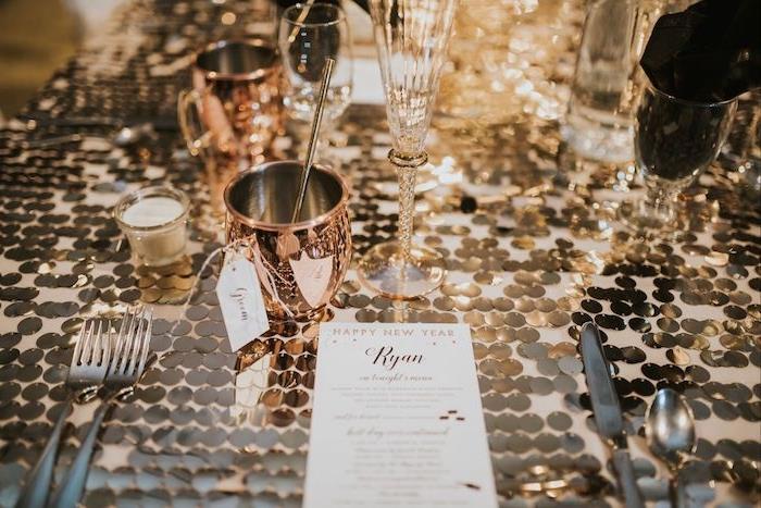 Novoletna dekoracija mize s kovinsko zlatimi detajli mize, okrasnimi svečami in kozarci iz rožnatega zlata, srebrnim priborom