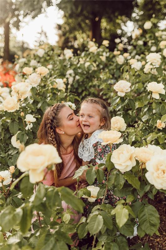 Mama ir dukra su ta pačia šukuosena, pynimo šukuosena, šukuosena mergaitei, vaiko šukuosena, nuotrauka sode tarp rožių