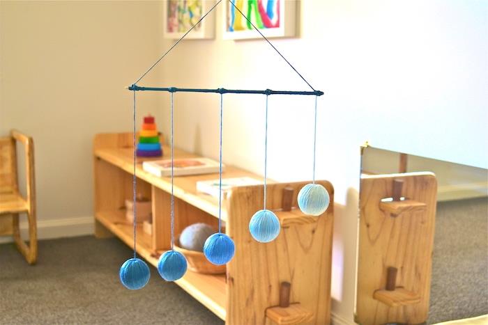 „Montessori“ mobilusis telefonas pakabinti vaikų kambaryje, pavyzdys berniuko „Montessori“ kamuolys mėlynuose rutuliuose, mediniai baldai