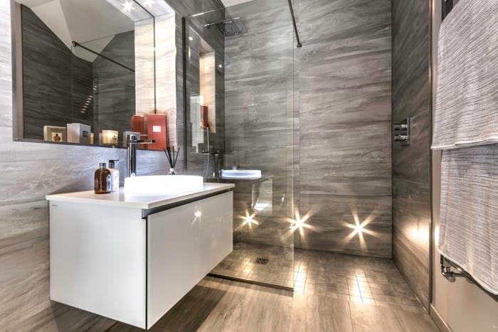 model tuš kabine s stekleno steno in sivimi ploščicami, dekoracija majhne kopalnice v sivi barvi z belo omarico
