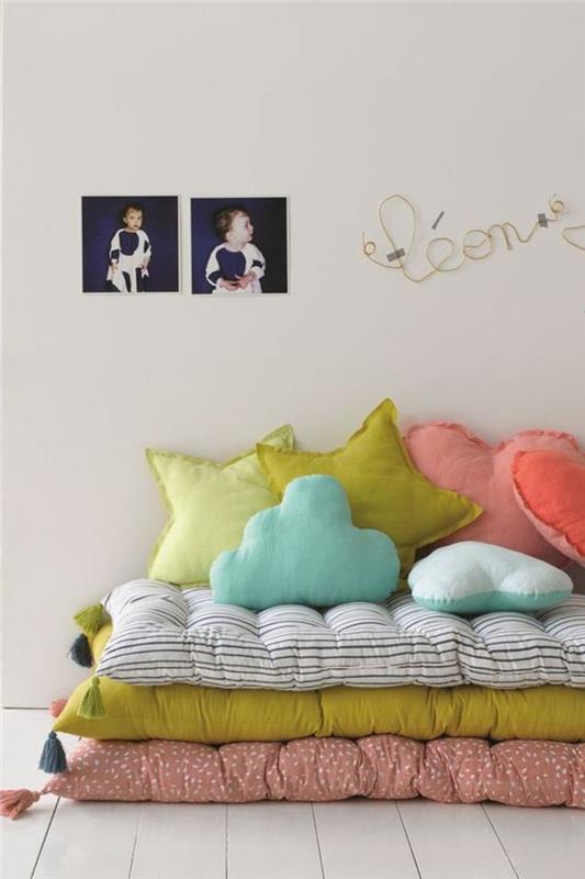 postelja montessori, spalnica montessori, pohištvo montessori, tri barvne vzmetnice postavljene ena na drugo, jaslice brez palic, bež stene, blazine v roza barvi in ​​resede v obliki zvezd