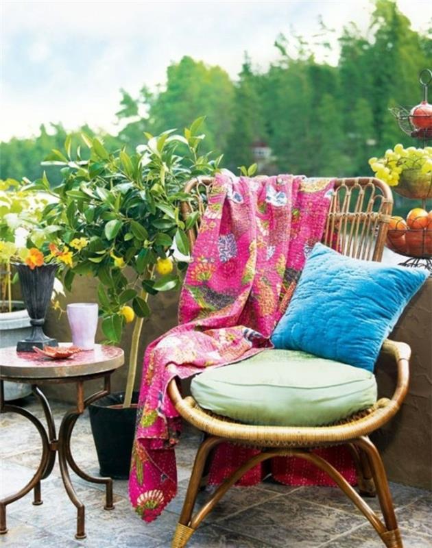 tkani stol, okrašen z modro blazino, okrogla klubska mizica na rjavi in ​​sivi popločani terasi, eksotične rastline