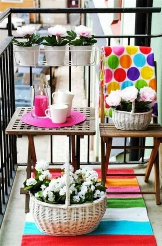 lesena miza in stol, rastline v belih lončkih, cvetlična košara na pisani črtasti preprogi, oblikovalska terasa