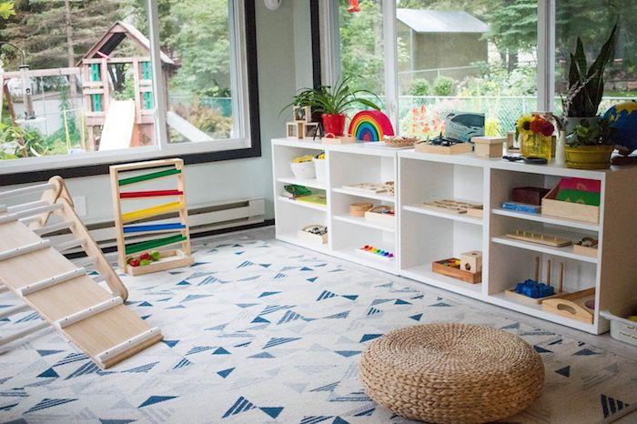 namų žaidimų aikštelė su Montessori žaislais, mėlynos ir pilkos spalvos trikampio kilimėliu, žema žaislų lentyna, jūros žolės osmanu