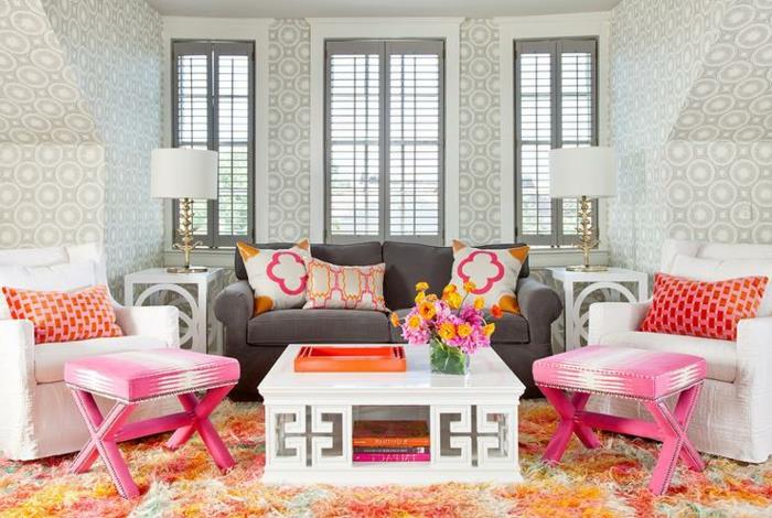 pilka spintelė, oranžinis kilimas, stačiakampis baltas stalas, rausvos išmatos, spalvingos pagalvėlės