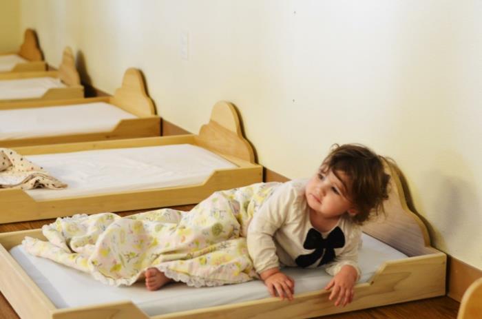 postelja iz koče montessori, pohištvo montessori, soba montessori, šest postelj iz svetlega lesa v vrtcu, štiriletni otrok vstaja iz postelje