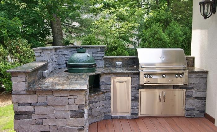virtuvės modelis, įrengtas terasoje su rudomis medinėmis grindimis su akmenine sala ir nerūdijančio plieno kepsnine