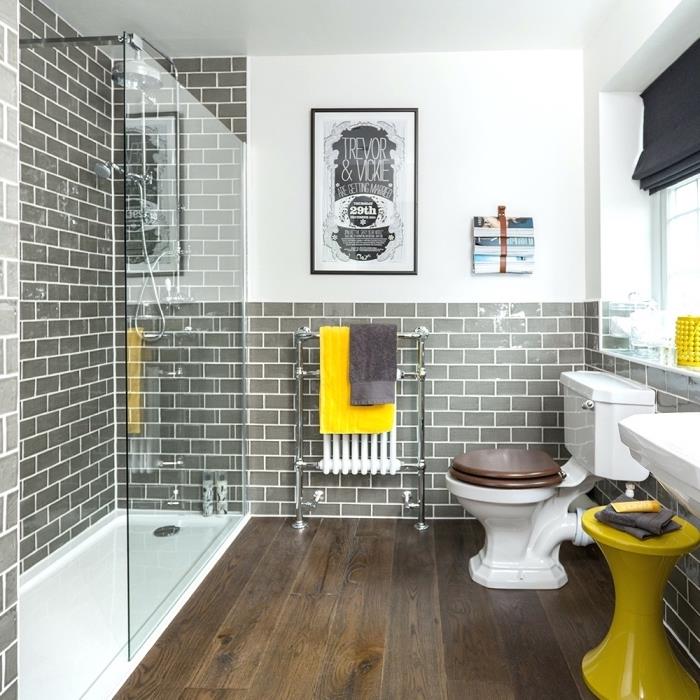 sivo -bela kopalnica s ploščicami iz sive opeke in podom iz temnega lesa, dekoracija z rumenimi dodatki