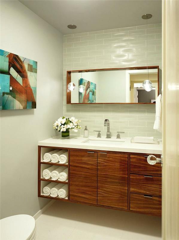 modernus tualeto išdėstymas, medinė spintelė, stačiakampis veidrodis, metro plytelės, abstrakti tapyba, suvynioti rankšluosčiai
