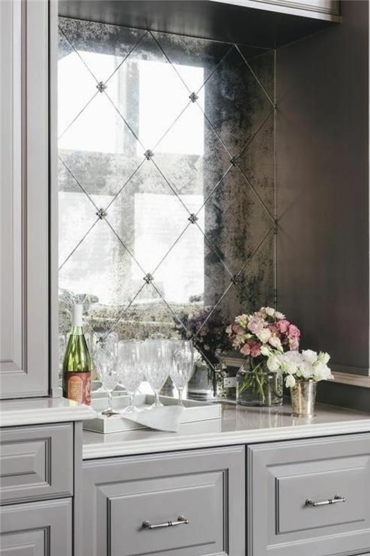 moderno opremljena kuhinja, postavitev kuhinje, starinsko ogledalo s staranim učinkom, kot, okrašen s steklenico vina, dvema kozarcema in cvetjem v beli in roza barvi, bela delovna plošča