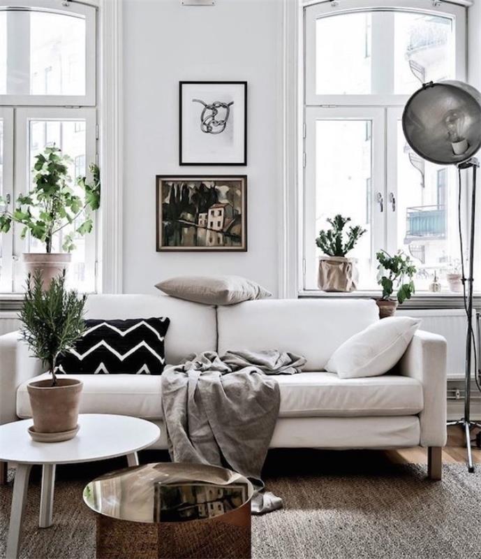 Beyaz kanepe, gri battaniye ve siyah, beyaz ve gri dekoratif minderler, beyaz sehpa, beyaz duvar, yeşil bitkiler dekoru ile İskandinav tarzı dekor