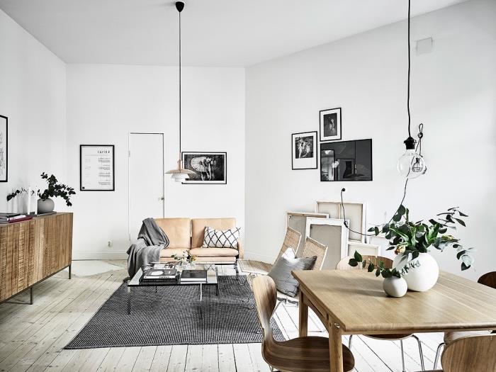 Oturma odasında İskandinav mobilyaları, deri koltuklu kanepe, siyah beyaz halı, yemek alanında ahşap masa ve sandalyeler, açık gri parke, grafik duvar dekorasyonu