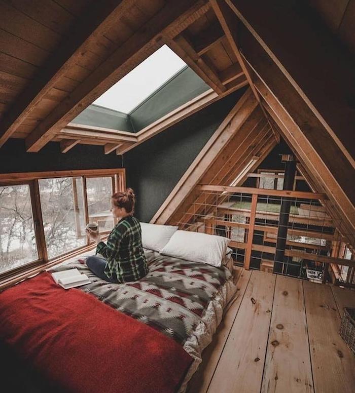 Ženska, ki sedi na postelji s knjigo in skodelico kave, deco v planinski koči, skandinavski leseni okras