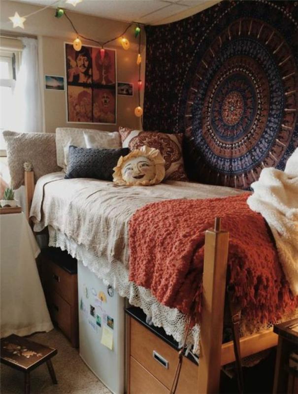 10 kvadratinių metrų ploto miegamojo išplanavimas hippi stiliaus, „boho“ prašmatnūs baldai, siena padengta audiniu su mandalos raštais, mažas baltas šaldytuvas po lova, įvairiaspalvių lempučių girlianda, kabanti nuo lubų
