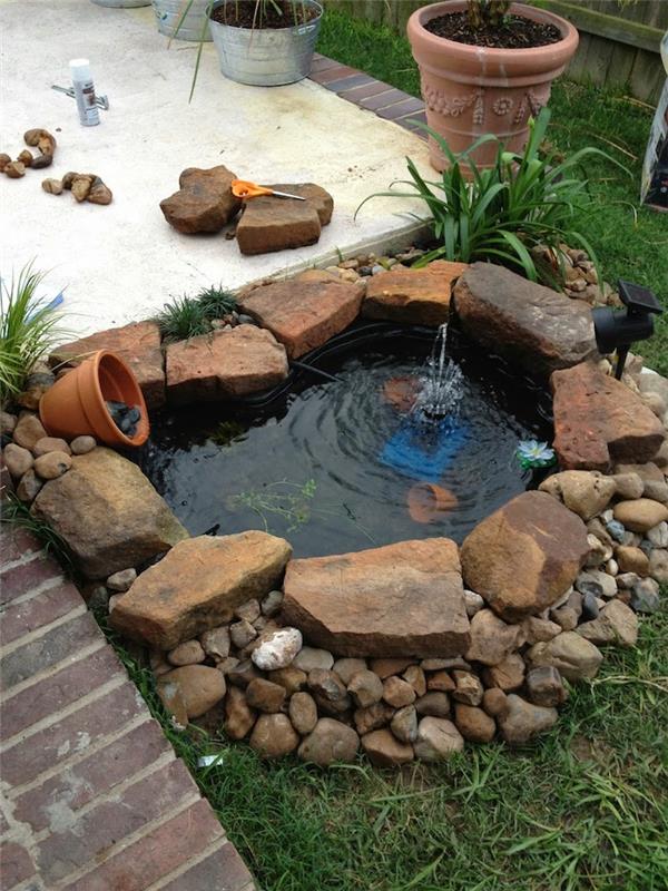 Bahçede saksı ve su bulunan çakıl taşları ve daha büyük taşlarla çevrili mini bahçe göleti