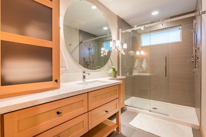medžio ir balto vonios kambario dizainas su dušo kabina, maža vonios kambario apdaila su dideliu apvaliu veidrodžiu ir gėlėmis