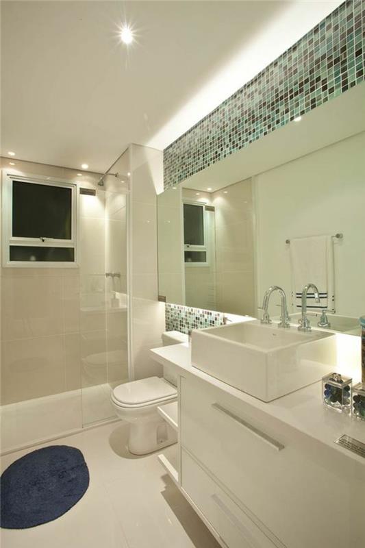 Aynanın üstünde ve altında vurgular olarak yeşil ve koyu gri mozaiklere sahip parlak banyo aynası