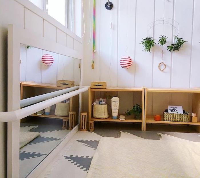 montessori veidrodis ant horizontalaus, pilko ir balto kilimo, žemos lentynos ant grindų, baltos dailylentės, originali sienų apdaila