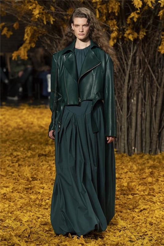 manekenka, ki hodi po preprogi iz jesenskega listja, oblečena v temno zeleno obleko, jesenski modni trendi, temno zelena usnjena jakna