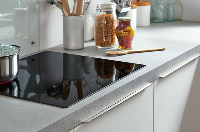 črna peč v belo lakirani kuhinji, siva delovna plošča in bela podlaga, dobro organiziran kuhinjski kotiček