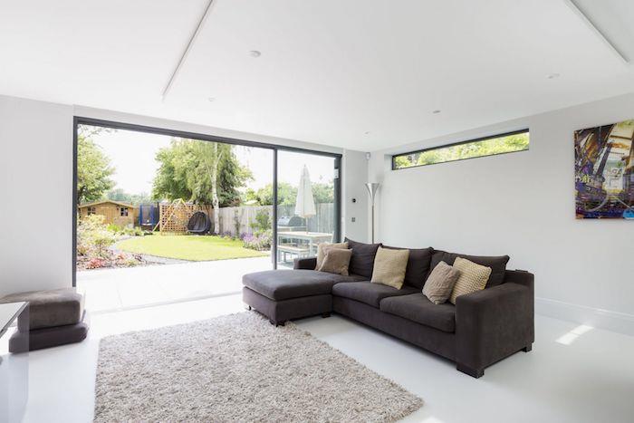 baltos sienos ir minimalistinio stiliaus prabangus garažo priestatas su šviesiai pilku kilimu ir tamsiai pilka sofa