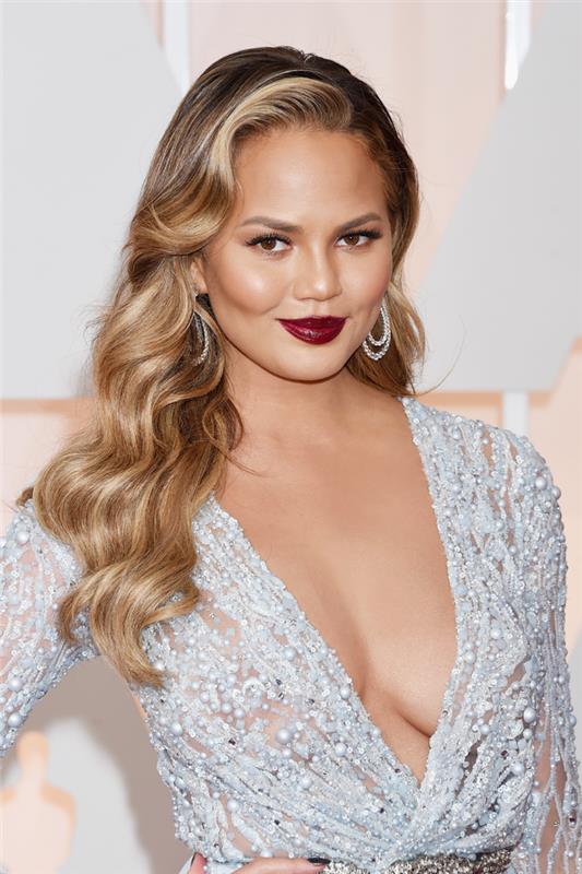 chrissy teigen šukuosena raudonam kilimui, makiažo ir šeštojo dešimtmečio stiliaus šukuosena, didelės garbanos, ilga balta suknelė