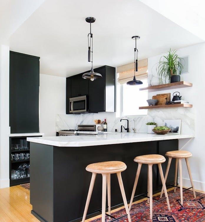 matinis juodas l formos virtuvės modelis su baltais stalviršiais, rytietiškas kilimas, medinės kėdės, medinės lentynos, pramoniniai pakabinami žibintai