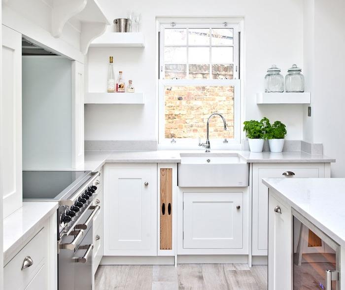maža balta virtuvė su baltu fasadu ir perlamutriniu stalviršiu, baltos sieninės lentynos, nerūdijančio plieno viryklė