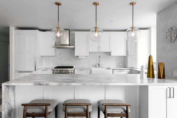 mermer efektli duvarlar ve sıçramalı beyaz ve şık mutfak, adalı mutfak dekoru, altın aksesuarlı örnek beyaz mutfak