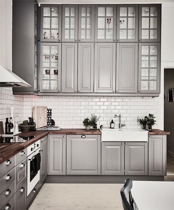 įrengta virtuvė su pilkais aukštais ir žemais baldais, baltos spalvos plytelėmis, tamsios medienos stalviršis