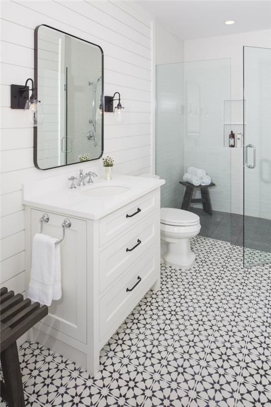 italų vonios kambario modelis, kuris savo medžiaginiais efektais žaidžia su cementinėmis plytelėmis išklotomis grindimis, stikliniu dušo ekranu ir dailylentėmis