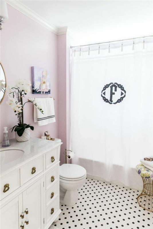 mažas vonios kambarys su balta spintele su retro stiliaus rankovėmis ir monograminėmis dušo užuolaidomis