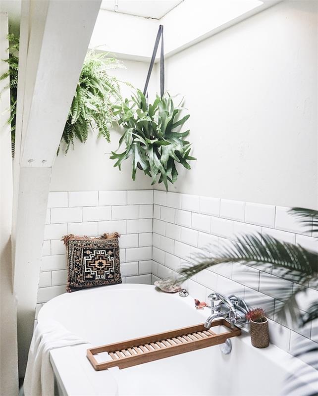 Zen kopalnica v duhu dekorja džungle z visečimi zelenimi rastlinami v lončkih, bela kad, podlaga iz belih ploščic, orientalska okrasna blazina