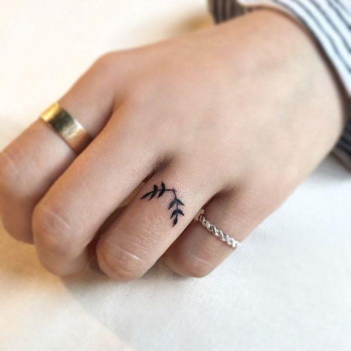 moteriško piršto tatuiruotė su diskretišku ir moterišku dizainu, vaizduojančia dvi mažas šakas, tatuiruotes kaip žiedas ant bevardžio piršto