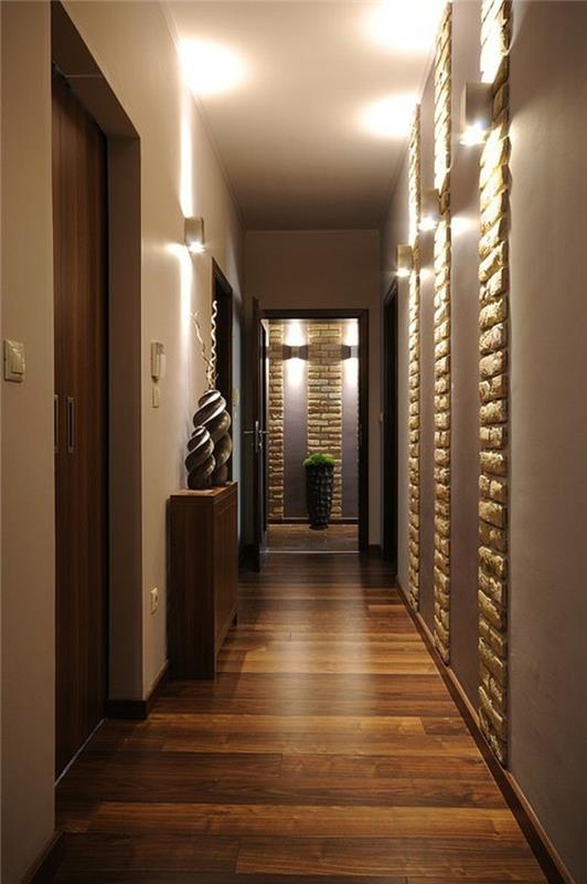 razkošna minimalistična dvorana z lesenimi deskami, vgrajenimi kamnitimi detajli v stenah, oblikovalskimi idejami hodnika, lesenimi vrati, dvema skulpturama na rjavi omari, lončnico v ozadju