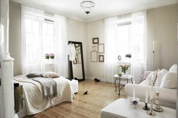 Arredare başına una soluzione monolocale con un divano bianco, pareti e tende bianche, parke chiaro ve specchio con korniş nera
