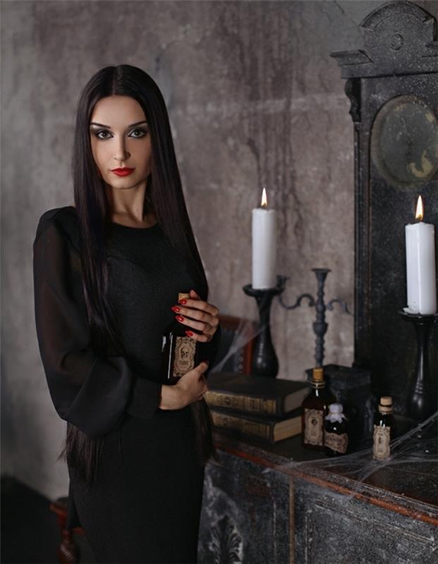 Morticia Addams aprangos idėja, juoda suknelė permatomomis rankovėmis, grimoire knygos, žvakių flakonai fone, ilgi lygūs plaukai šviesiai atspalvis