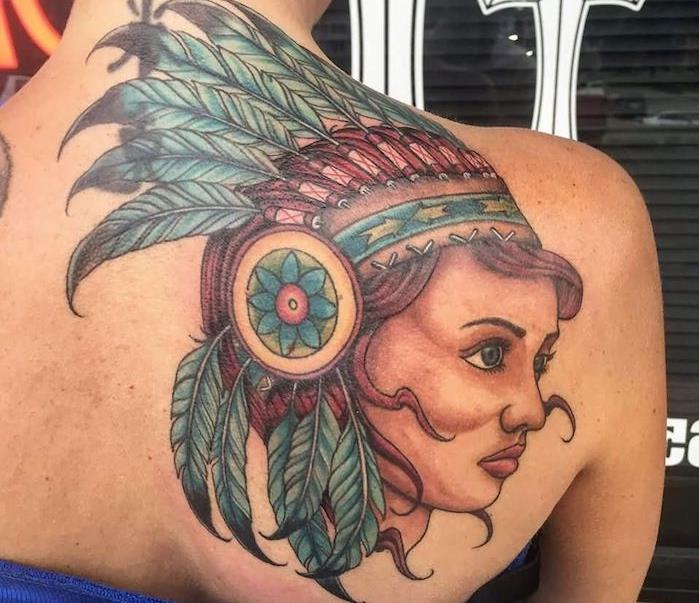 ameriška indijska tetovaža, body art na ženskem hrbtu z ženskim obrazom z rdečimi lasmi in modrim perjem