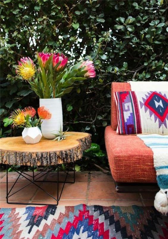 Actekų motyvai, oranžinė sofa, medžio kamieno stalas, vazos su gėlėmis, raudonos ir mėlynos spalvos kilimas