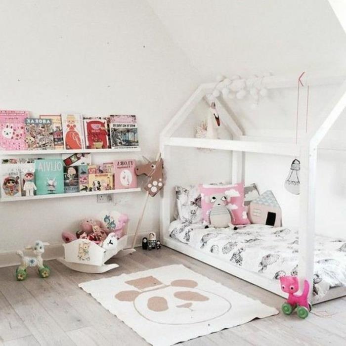 kūdikio kambario išdėstymas pagal Montessori metodą, pandos kilimas, balta žaidimų namų lova, knygų lentynos, pagalvėlės
