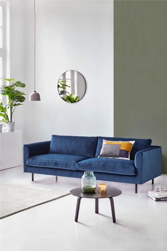 beyaz, yeşil ve mavi bir oturma odasında doğal ve rahatlatıcı bir atmosfer, gri, hardal sarısı ve çivit mavisi baskılı minder ile vurgulanan tasarımcı lacivert kanepe