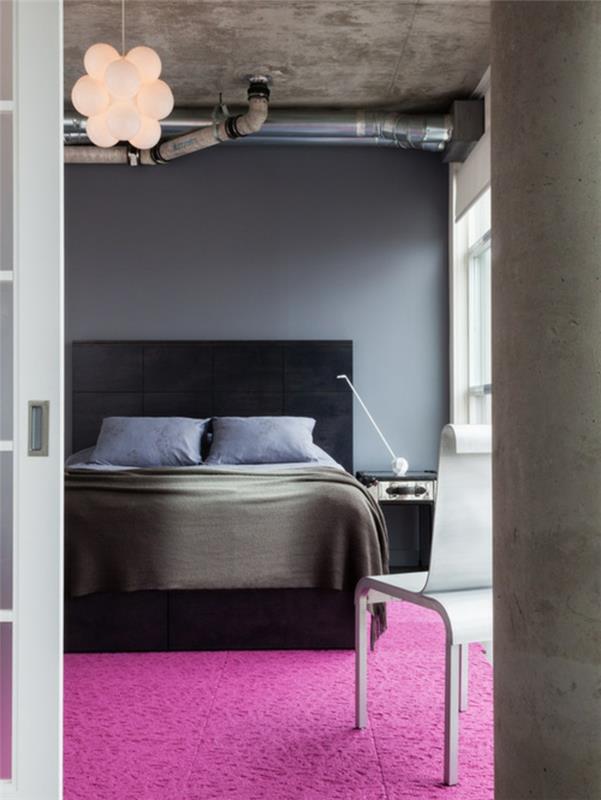 roza in siva spalnica, ogljeno siva stena, temno siva postelja, modra in siva posteljnina, magenta roza preproga, betonski strop in cevi v industrijskem slogu