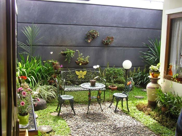 gramozna betonska ograja stena kovinska miza in stoli zelena trava grmičevje in rastline