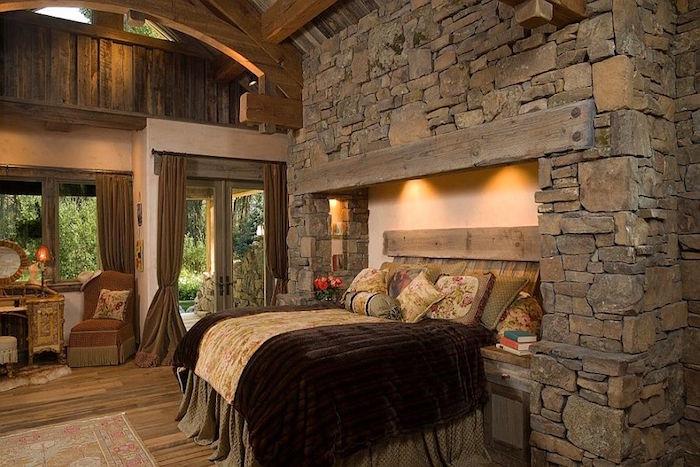 viduramžių pilies stiliaus miegamasis su senomis pilkomis akmens sienomis, skirtingomis formomis ir lova židinio rėme ir mediniame rėme