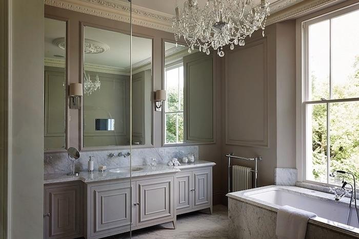 svetlo siva stena s sivo kuhinjsko omarico in marmorno delovno površino, samostojna kad, baročni lestenec, ogledala