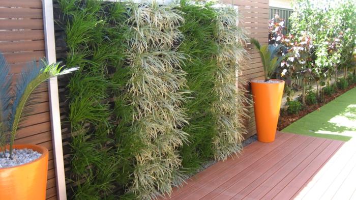vertikalus sodas, kolonų plokštės su žaliais augalais, du kūgio formos sodinamosios oranžinės spalvos su palmėmis, žalia siena