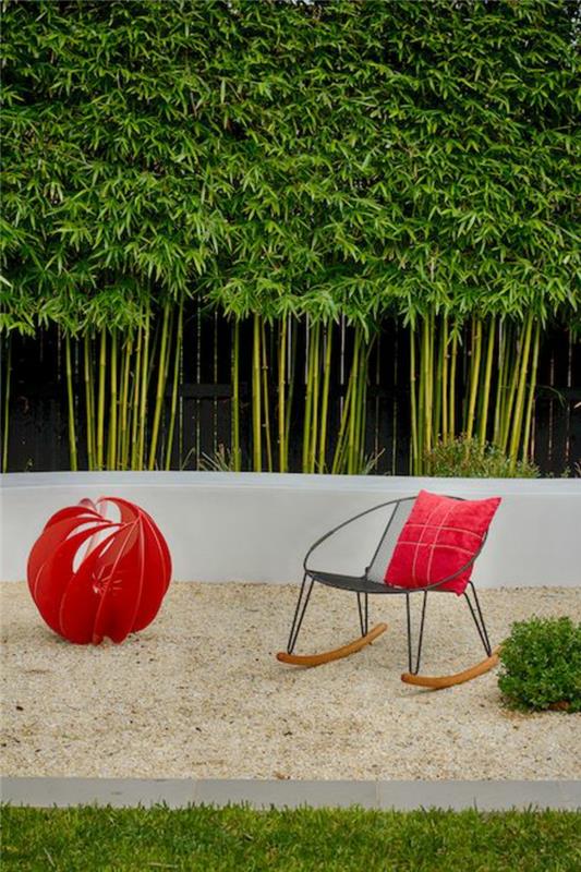 bambu saplı bitki bölmesi, siyah metal ve hafif ahşap koltuklu rahat bahçe köşesi, kırmızı kumaş top, tasarım dekorasyonu, ince kum, bakımlı yeşil çimen, dış mekan bitki duvarı