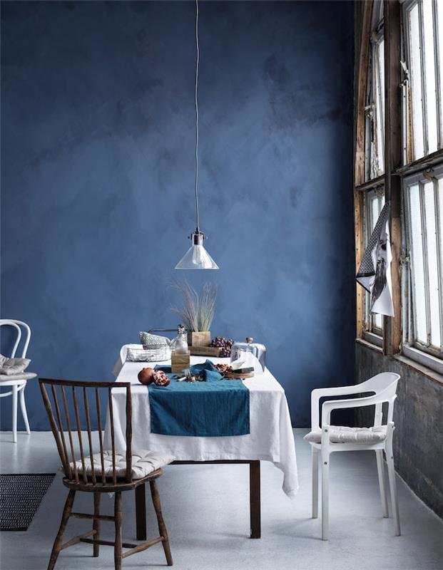 sodobna jedilnica v temno modri barvi, bela tla in prt na leseni mizi, velika okna, nizka viseča svetilka