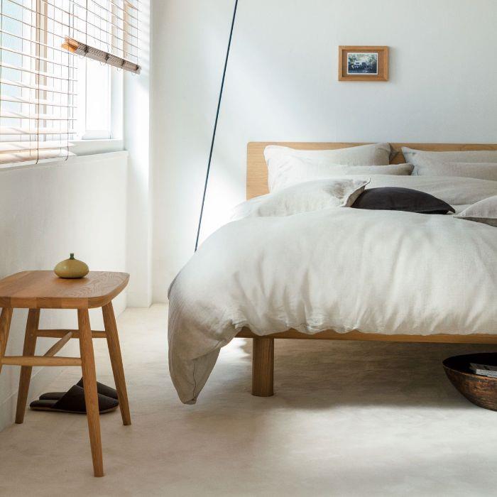 bele stene in tla belo posteljnino na leseni postelji in leseni nočni omarici primer japonske spalnice v minimalističnem slogu